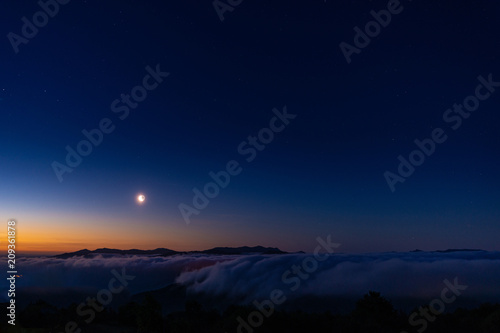 Quarto di Luna nel cielo sereno all’alba sopra una distesa di nuvole bianche