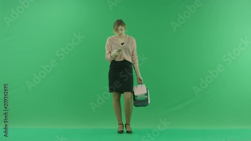 Pretty shopping woman is surfing the internet with shopping bags. Female shopper holding shopping bags front on green background in studio. photo