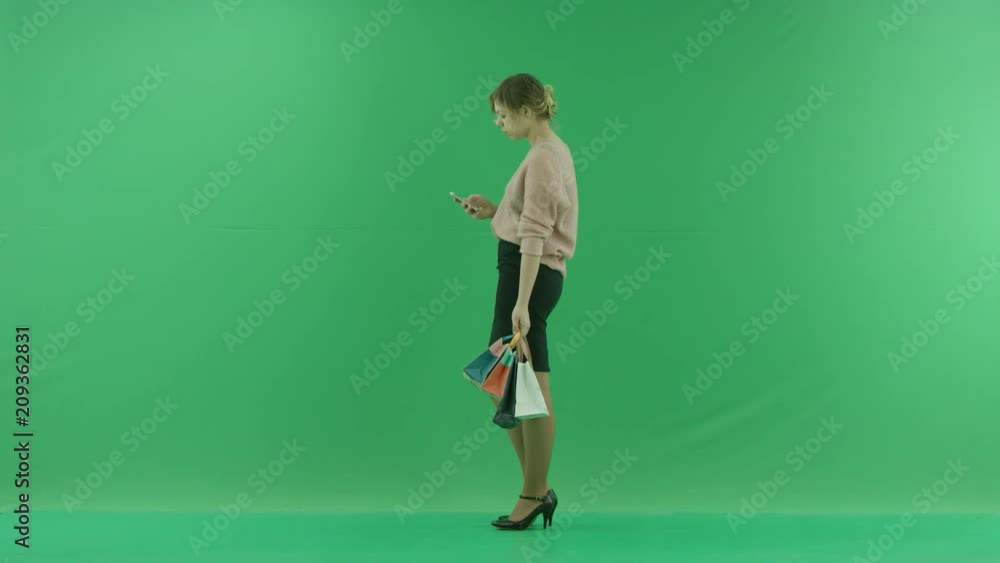 Pretty shopping is surfing the internet woman with shopping bags. Female shopper holding shopping bags sideways on green background in studio. Pretty shopping is surfing the internet woman with shopping bags. Female shopper holding shopping bags sideways on green background in studio.