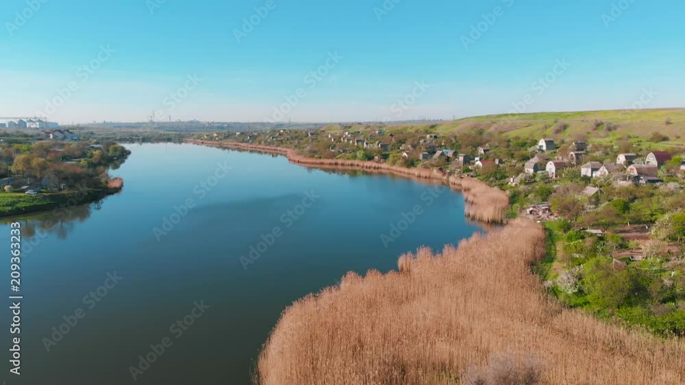 The flight of drones over country houses in the hills on the shore of the pond early in the morning at dawn. Flight over the water at a bird's eye view. Aerial view 4K The flight of drones over country houses in the hills on the shore of the pond early in the morning at dawn. Flight over the water at a bird's eye view. Aerial view 4K