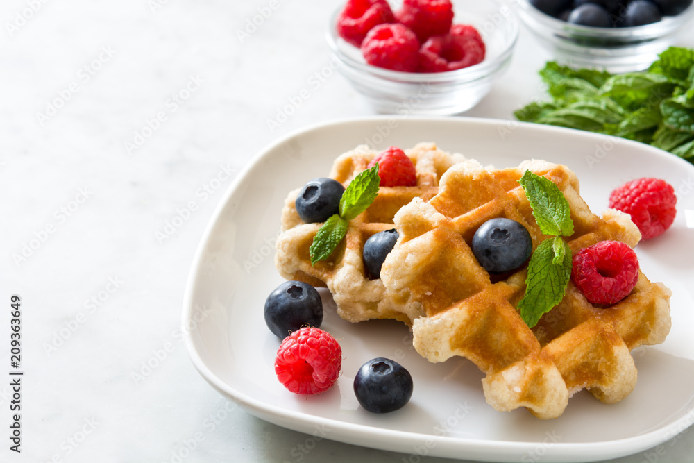 Traditional belgian waffles with blueberries and raspberries on white marble Traditional belgian waffles with blueberries and raspberries on white marble