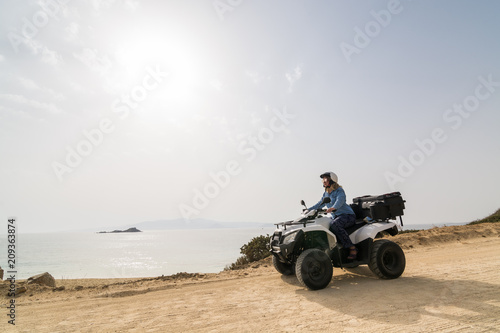 Young woman driving rental ATV quad bike on seaside road in Naxos island, Greece