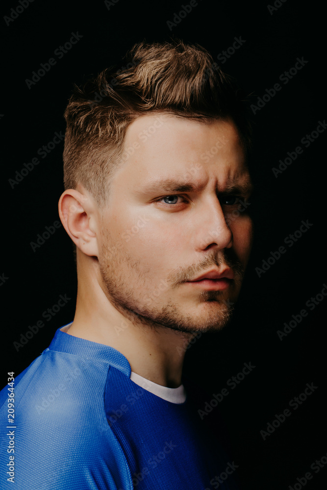 Obraz premium Close-up portrait of young handsome football player soccer posing on black dark background.