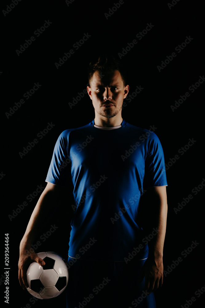 Young soccer player with ball on black background in studio.