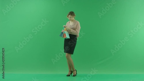 Pretty shopping woman is surfing the internet with shopping bags. Female shopper holding shopping bags sideways on green background in studio. photo