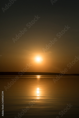 Orange golden colorful sunset above the lake with calm water surface with a horizont line © Kseniia