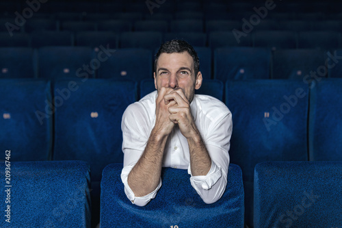 portrait of young man alone at the cinema making expressions of amazement, fear for the movie he is watching