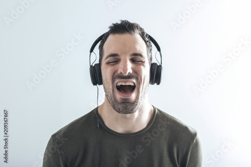 young man on a white background sings his favorite song while listening to music with headphones