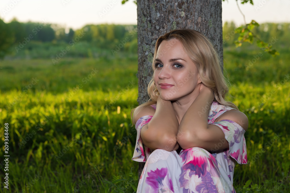 A girl with light wavy hair sits by a tree in the park A girl with light wavy hair sits by a tree in the park