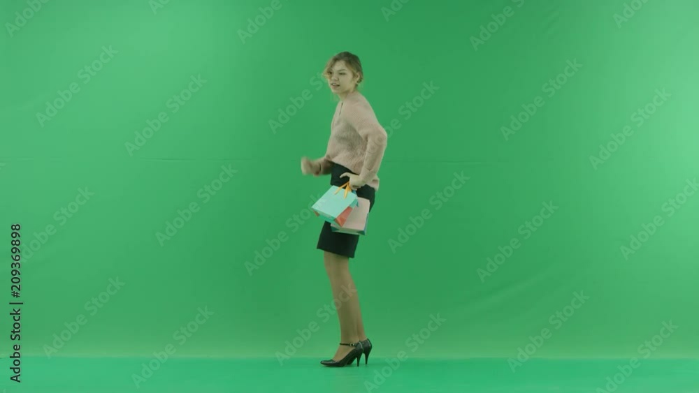 Pretty shopping woman is dancing with shopping bags. Female shopper holding shopping bags sideways on green background in studio. Pretty shopping woman is dancing with shopping bags. Female shopper holding shopping bags sideways on green background in studio.
