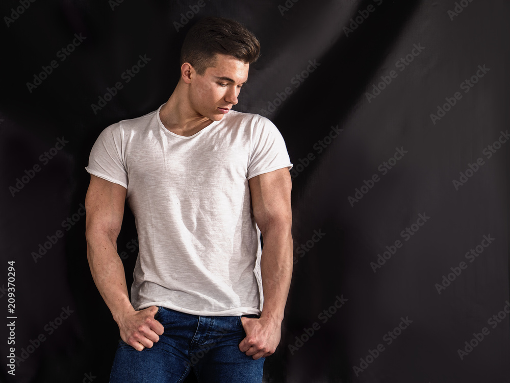 Handsome young muscular man looking down to a side, in studio shot over neutral dark background Handsome young muscular man looking down to a side, in studio shot over neutral dark background