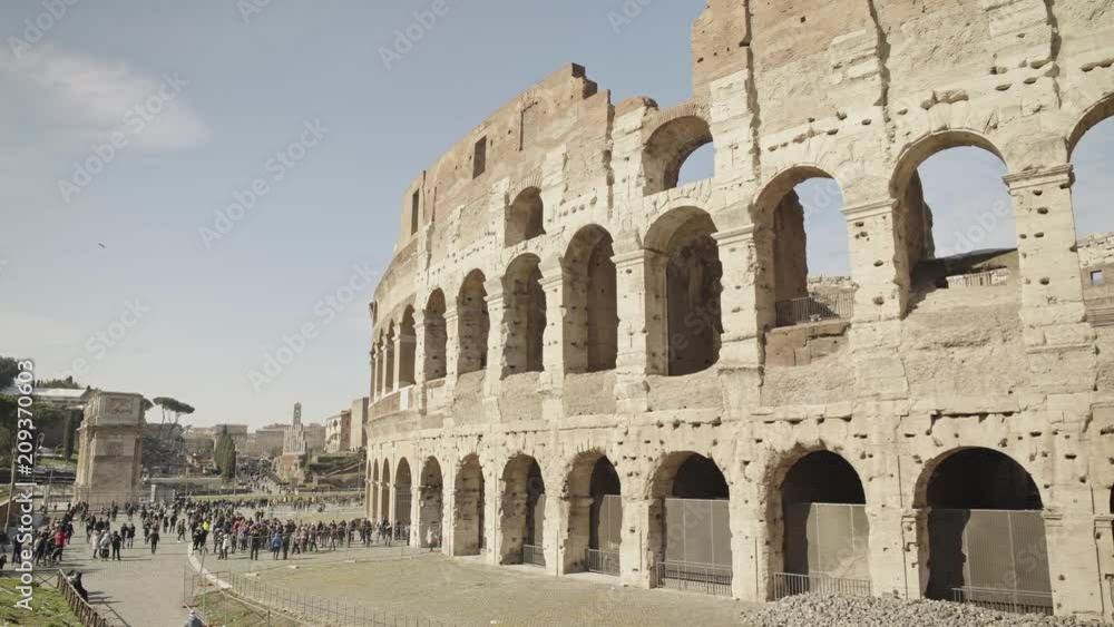 ROME - FEB 20: Crouds of tourists near Roman Colosseum Coliseum Flavian Amphitheatre Anfiteatro Flavio Colosseo,a former gladiator arena. Cars and traffic signs. Summer day. Left to right pan shot ROME - FEB 20: Crouds of tourists near Roman Colosseum Coliseum Flavian Amphitheatre Anfiteatro Flavio Colosseo,a former gladiator arena. Cars and traffic signs. Summer day. Left to right pan shot