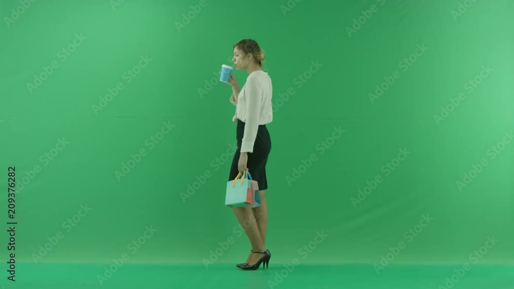 Pretty shopping woman is drinking coffee from paper cup with shopping bags. Female shopper holding shopping bags sideways on green background in studio. Pretty shopping woman is drinking coffee from paper cup with shopping bags. Female shopper holding shopping bags sideways on green background in studio.