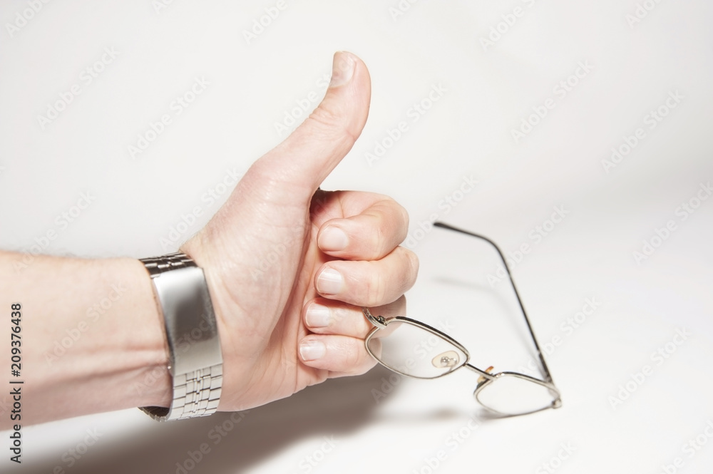 A hand on a gray background holds glasses for better vision and shows the class with a thumb A hand on a gray background holds glasses for better vision and shows the class with a thumb