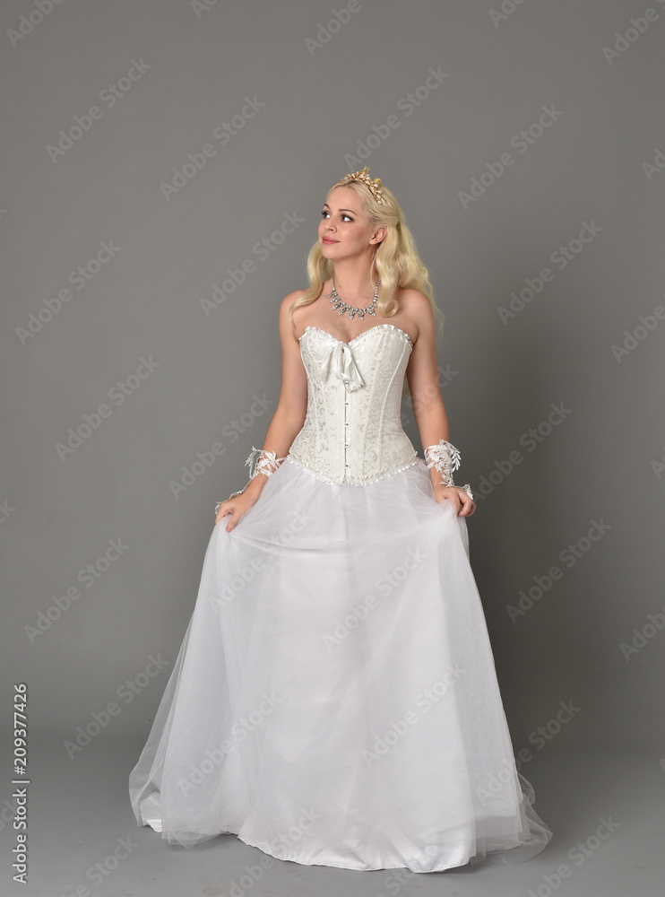 full length portrait of blonde girl wearing white corset gown. standing pose on grey studio background. full length portrait of blonde girl wearing white corset gown. standing pose on grey studio background.