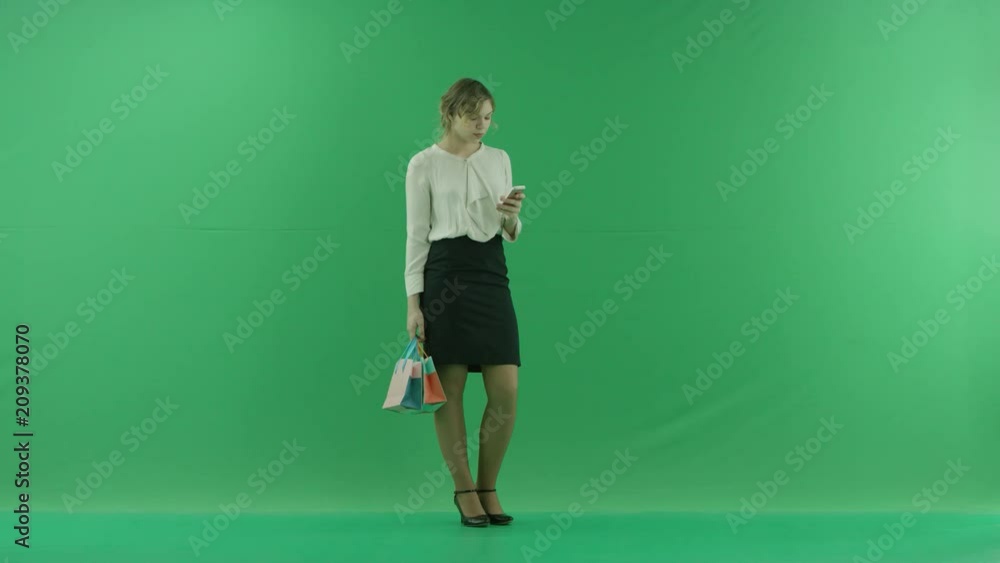 Pretty shopping woman is surfing the internet with shopping bags. Female shopper holding shopping bags front on green background in studio. Pretty shopping woman is surfing the internet with shopping bags. Female shopper holding shopping bags front on green background in studio.
