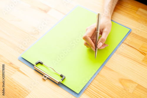 Office Hand Holding a Folder with a Green Color Paper and Pen on the Background of the Wooden Table. Copyspace. Place for Text.