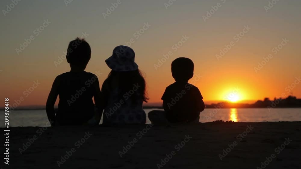 Two boys and a girl watching the sunset over the sea sitting on the beach Two boys and a girl watching the sunset over the sea sitting on the beach