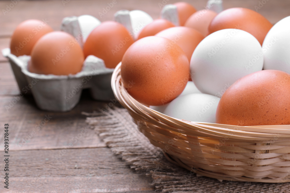Brown and white chicken eggs in a wicker basket next to the egg tray on a brown wooden background. Brown and white chicken eggs in a wicker basket next to the egg tray on a brown wooden background.