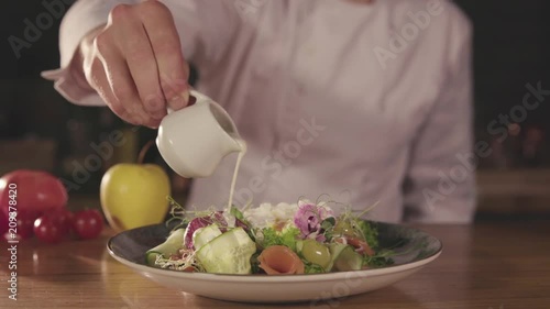 Chef Pours some white Sauce on a Slad with Fresh Chopped Vegetables. The dish looks tasty and colorful. Tomatoes , Apples are on the table. Modern and Appetizing Salad. photo