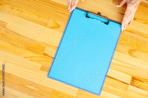 Office Hand Holding a Folder with a Blue Color Paper on the Background of the Wooden Table. Copyspace. Place for Text. photo