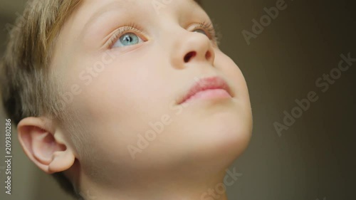 Close up of the cute blonde boy with blue eyse looking up at something. Lovely kid's face. Portrait shot. Indoor photo