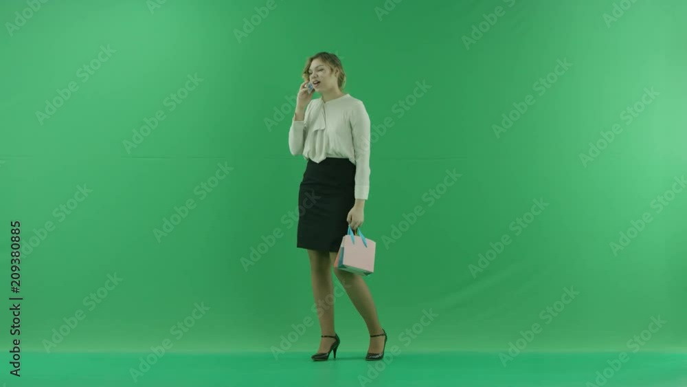 Pretty happy laughing shopping woman with shopping bags. Female shopper holding shopping bags sideways on green background in studio. Pretty happy laughing shopping woman with shopping bags. Female shopper holding shopping bags sideways on green background in studio.