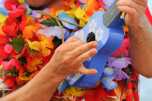 A man playing a Hawaiian ukulele wearing a bright flowered shirt