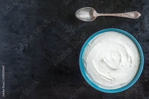 Greek yogurt with a spoon on a dark background top view