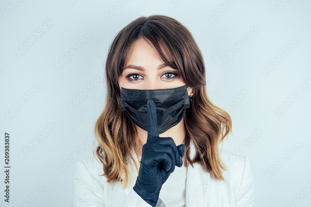 portrait of a beautiful and young doctor woman in white medical gown , black  rubber gloves and black mask on face on a white background. the concept of  silence and secret Stock-Foto