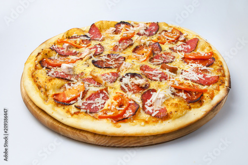 delicious pizza with bits of bacon and sausages is sprinkled with cheese and decorated with tomatoes is on a wooden board
