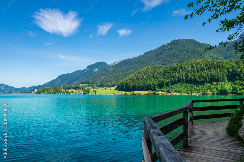 Steg entlang am See in Österreich welcher Wolfgangsee genannt wird mit Berge im Hintergrund und Wolken am Himmel