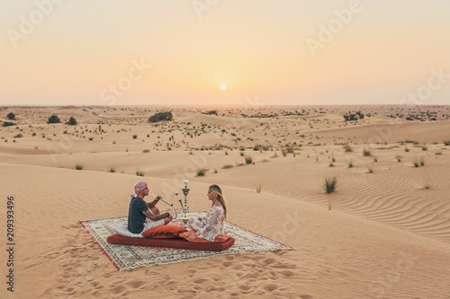 Romantic couple seating on a carpet in the Emirates desert 