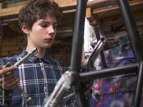 portrait of young man repairing the bmx bicycle holding instruments in garage