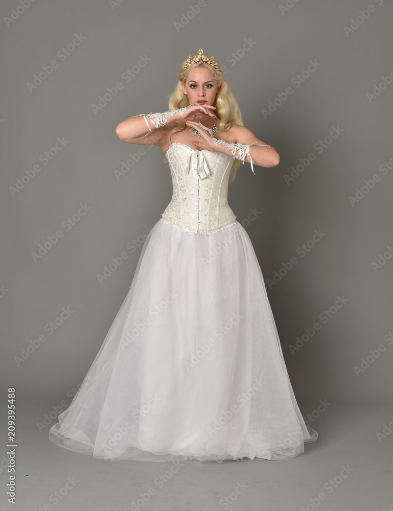 full length portrait of blonde girl wearing white corset gown. standing pose on grey studio background. full length portrait of blonde girl wearing white corset gown. standing pose on grey studio background.