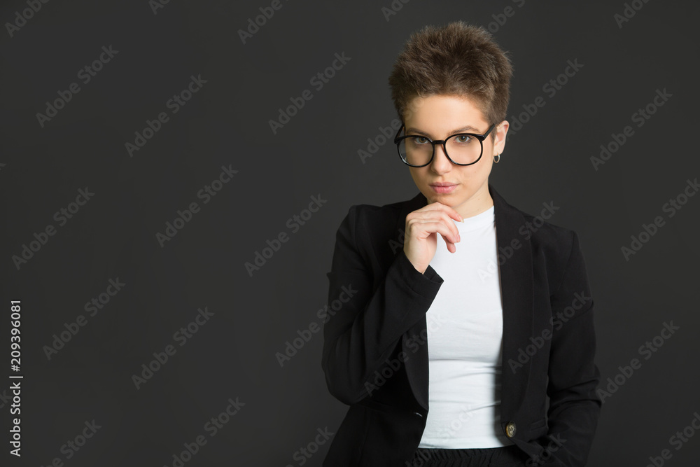 beautiful young girl with short hair, in a black suit and wearing glasses on a black background with a serious face beautiful young girl with short hair, in a black suit and wearing glasses on a black background with a serious face