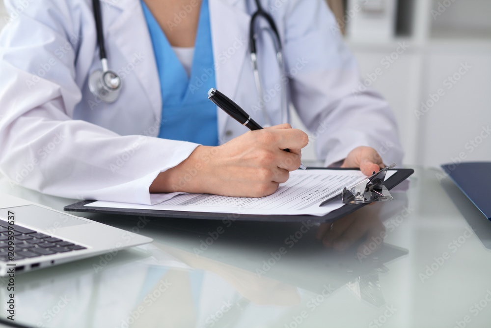 Fototapeta premium Doctor woman filling up medical form while sitting at the table, close-up of hands