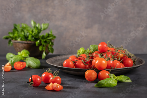 Small red cherry tomatoes on rustic background. Cherry tomatoes on the vine witb basil leaves photo