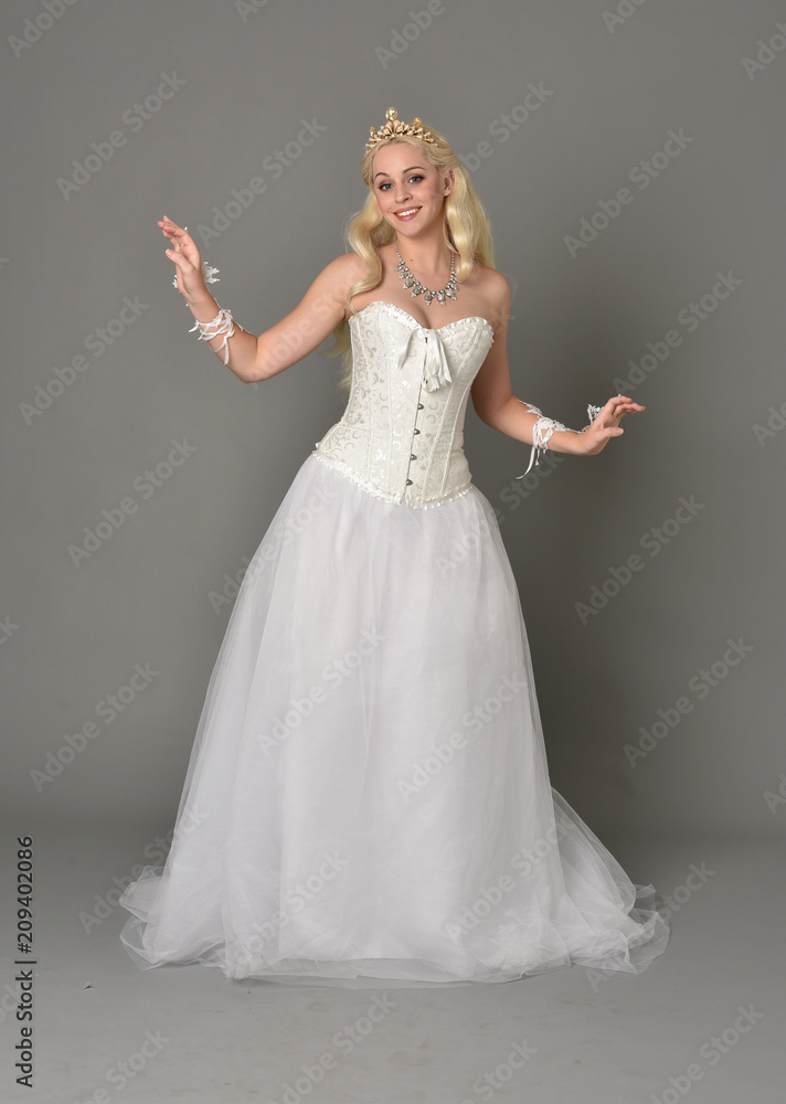full length portrait of blonde girl wearing white corset gown. standing pose on grey studio background. full length portrait of blonde girl wearing white corset gown. standing pose on grey studio background.