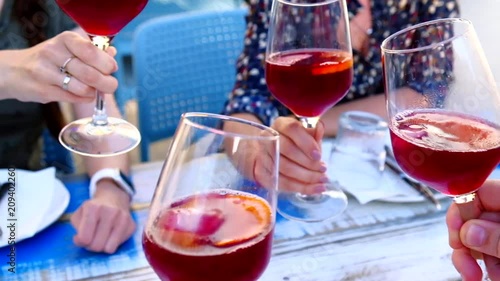 Group of friends clinking glasses with red wine sangria drink at outdoors restaurant. Drinking and leisure concept.
