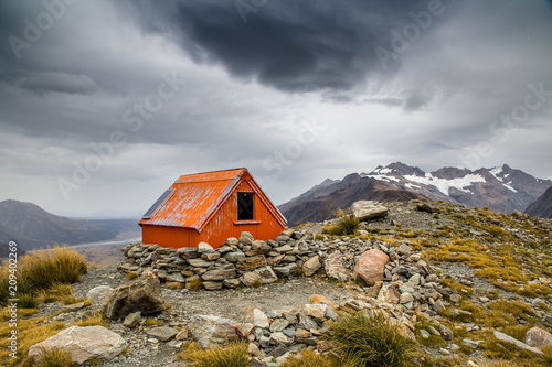 Mountain shelter red cabin high on a mountain side under stormy clouds