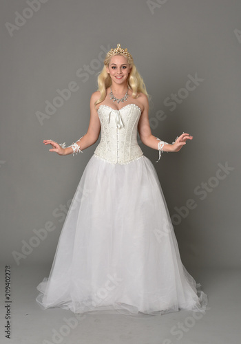 full length portrait of blonde girl wearing white corset gown. standing pose on grey studio background.