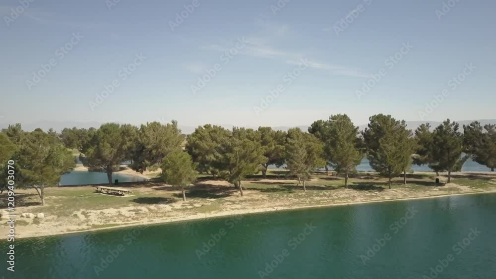 Island of trees surrounded by a vibrant blue lake – aerial pan Island of trees surrounded by a vibrant blue lake – aerial pan