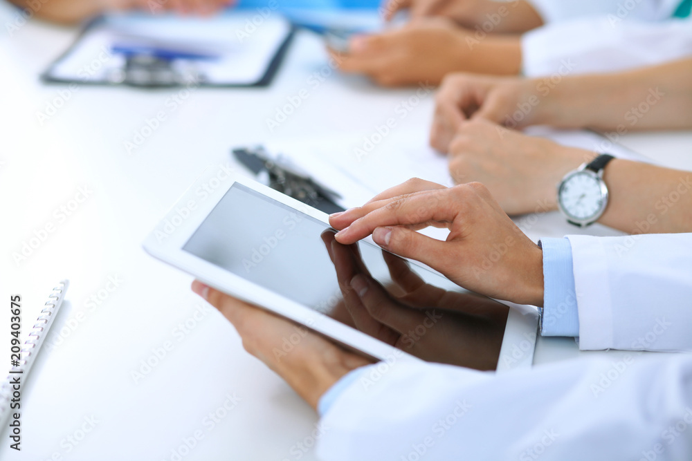 Fototapeta premium Doctor using tablet computer at medical meeting, closeup. Group of colleagues at the background