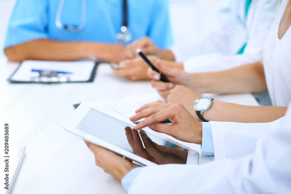 Doctor using tablet computer at medical meeting, closeup. Group of colleagues at the background Doctor using tablet computer at medical meeting, closeup. Group of colleagues at the background