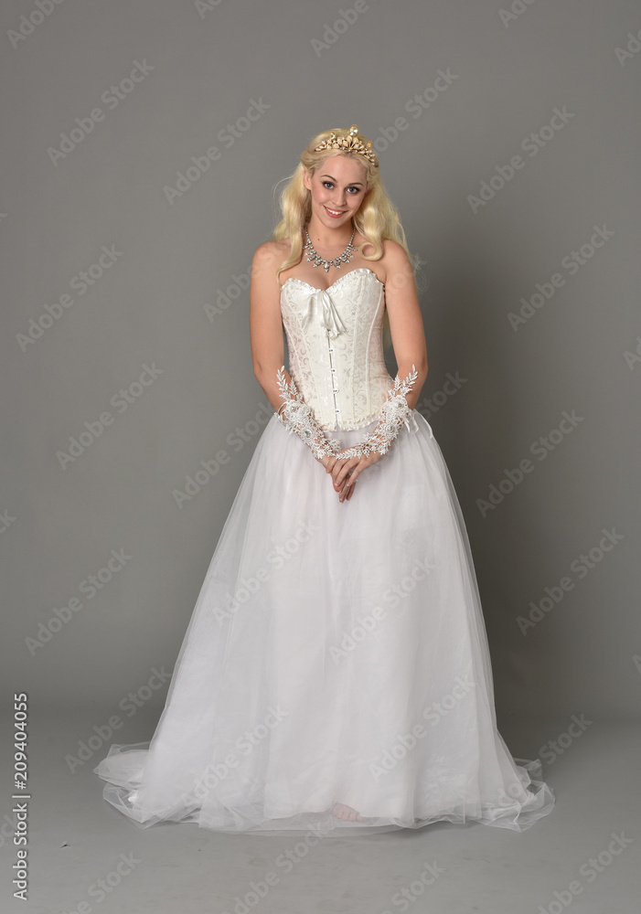 full length portrait of blonde girl wearing white corset gown. standing pose on grey studio background. full length portrait of blonde girl wearing white corset gown. standing pose on grey studio background.