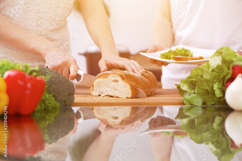 Closeup of human hands cooking in kitchen. Mother and daughter or two female friends cutting bread. Healthy meal, vegetarian food and lifestyle concept