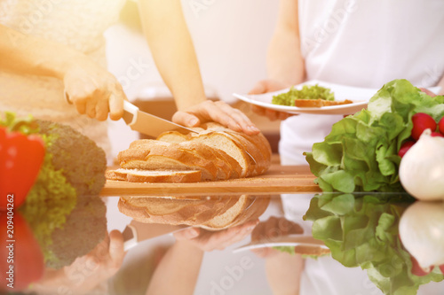 Closeup of human hands cooking in kitchen. Mother and daughter or two female friends cutting bread. Healthy meal, vegetarian food and lifestyle concept