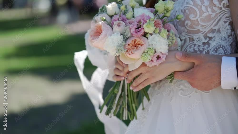 Young bride touching bridal bouquet in a park Young bride touching bridal bouquet in a park