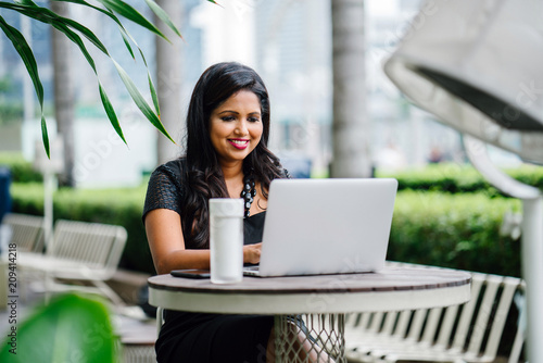 A confident and successful Indian woman (professional or business woman) is sitting and working on her laptop in the day. 